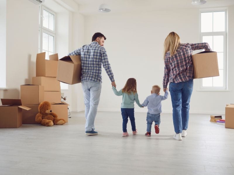 uomo, donna e bambino si tengono per mano in una casa con scatoloni a simbolo di un trasloco per affitto