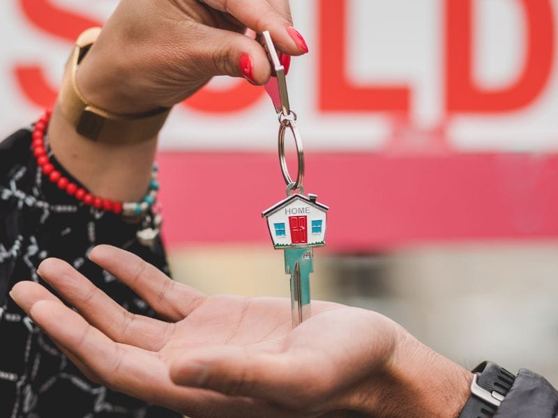 donna consegna chiavi di casa sullo sfondo cartello sold, venduta