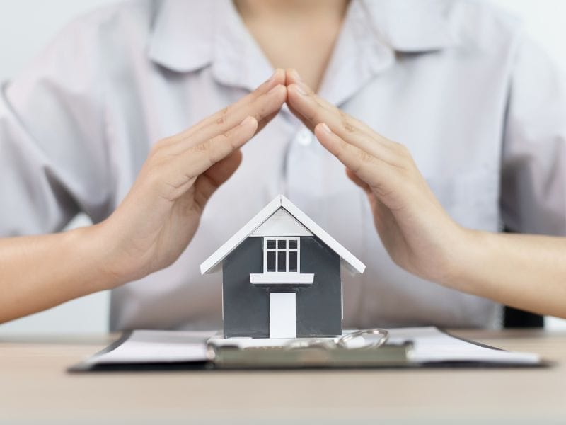 donna con mani a coppa su modelli di casa a simbolo della protezione che serve nell'acquisto di case indipendenti in vendita