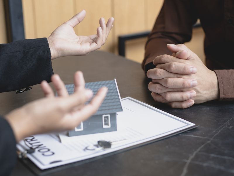 persone gesticolano sullo sfondo un modellino di casa