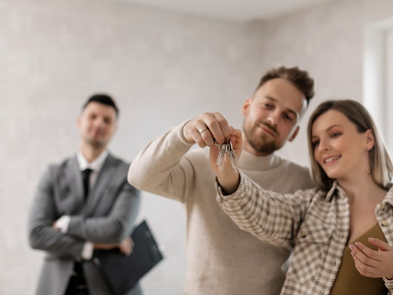 coppia tiene le chiavi di casa in mano, sullo sfondo un agente immobiliare